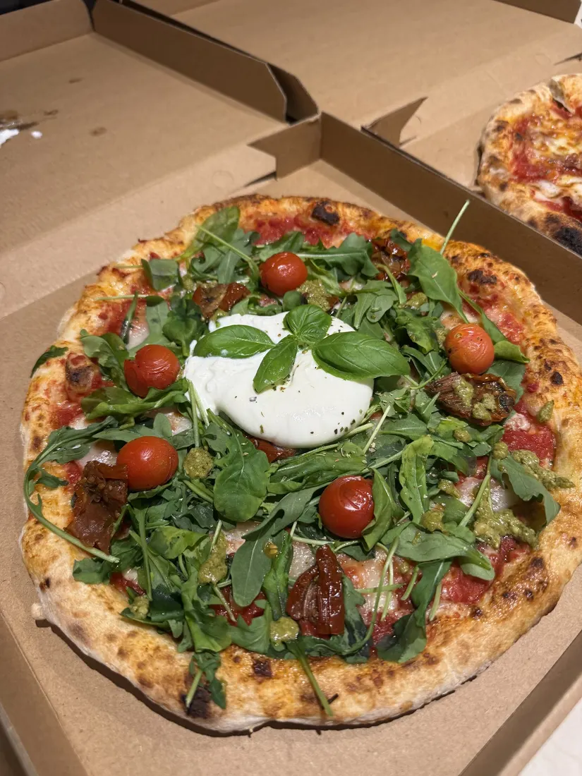 A pizza with burrata and rocket in its delivery box