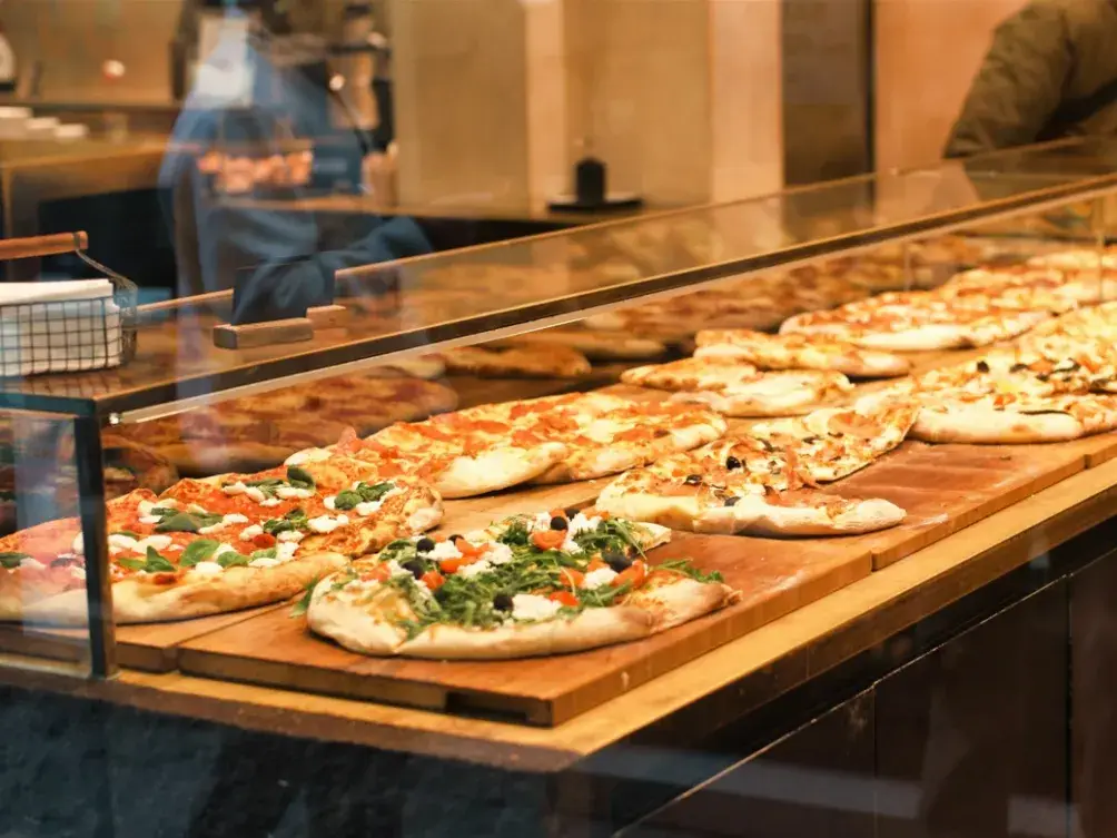 Pizzas served on long wooden boards at a counter
