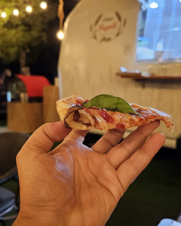 A guest holding a slice of pizza in front of the truck