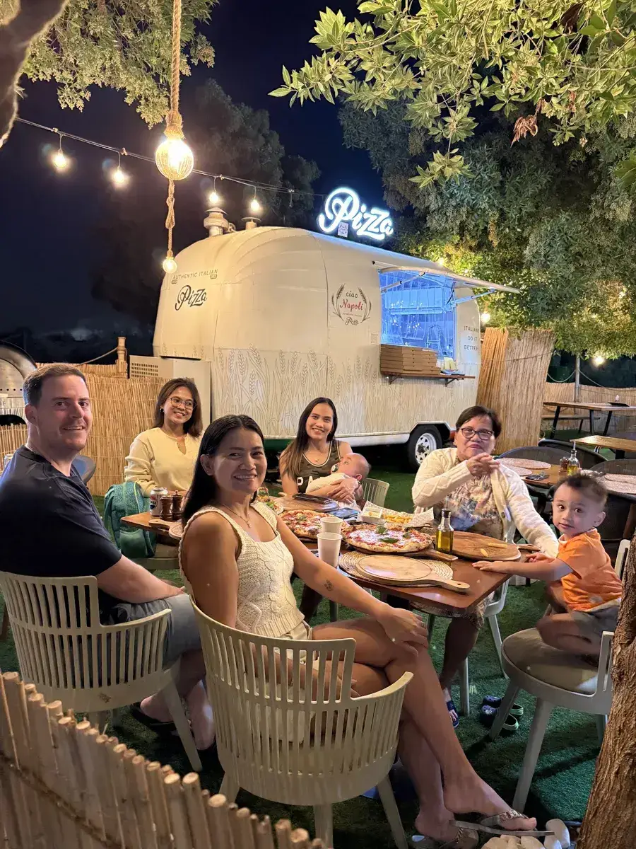 A family sharing pizzas at a table in front of the truck at night