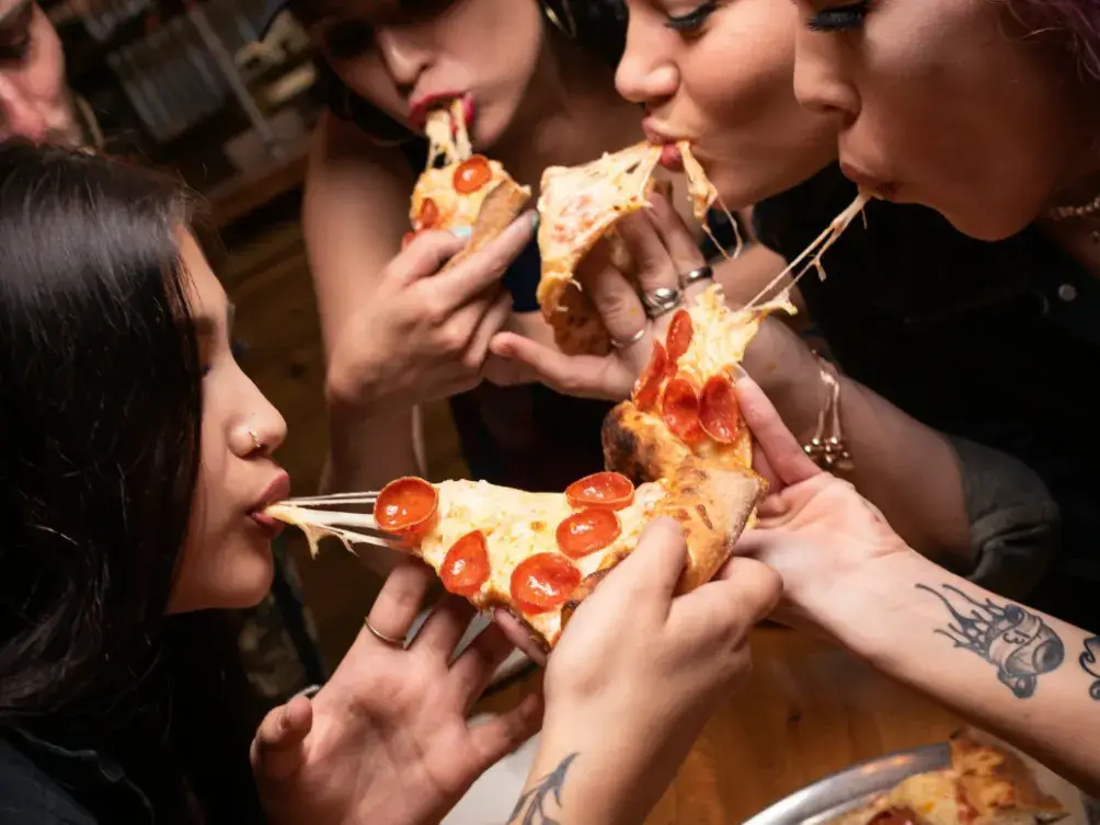 Friends biting into slices with stretchy cheese