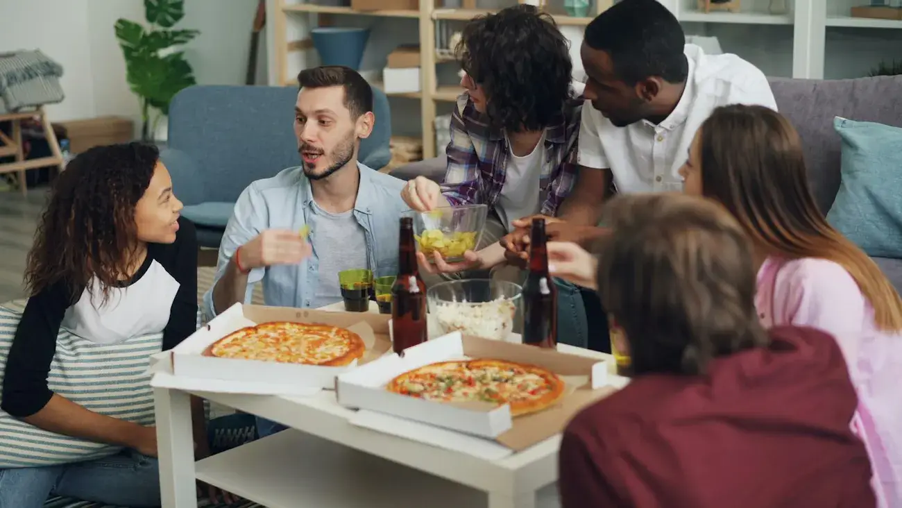 A group chatting around open pizza boxes on a low table